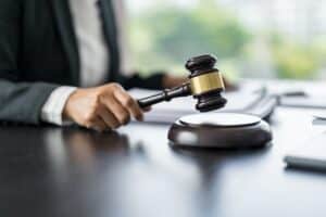 suited professional striking wooden gavel with gold band on sound block