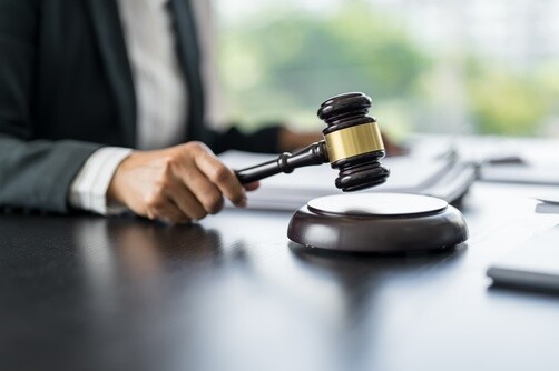 suited professional striking wooden gavel with gold band on sound block